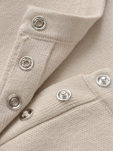 Details des beigen Strickpullovers mit feiner Textur und metallischen Druckknöpfen