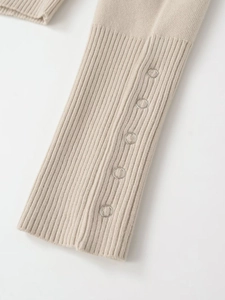 Detail eines beigen Strickpulloverärmels mit Rippbündchen und silbernen Metallringen