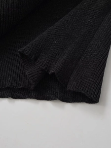 Close-up detail of premium black vertical ribbed knit texture on chic women's cape sweater