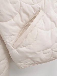 Close-up of floral quilted pattern and slanted pocket on cream jacket fabric