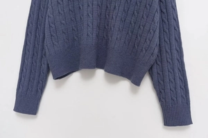 Detail of cable knit pattern and ribbed cuff on a blue long sleeve sweater