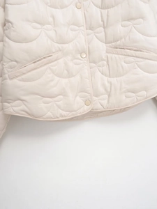 Detail of cream quilted jacket featuring unique bow pattern stitching and snap buttons