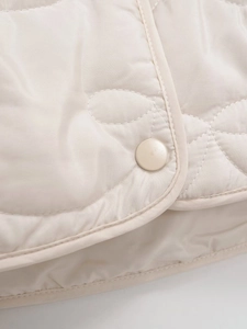 Detailed close-up of cream quilted jacket with wavy stitching and matching snap button