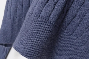Detail of indigo cable knit sweater showing textured rib cuffs and soft wool fabric