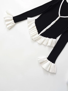 Détail d'un gilet en maille noir avec volants blancs et texture côtelée verticale