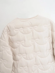 Detail of light beige quilted jacket showing unique bow-shaped stitching pattern