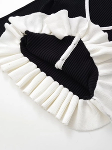 Détail du cardigan noir en maille côtelée avec bord volanté blanc et texture multicouche