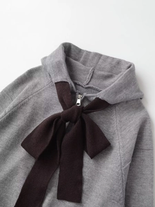 Detail of grey knit hoodie with dark brown bow accent and silver metal zipper