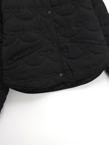 Detail of black quilted jacket with bow stitching, snap buttons and rounded hemline