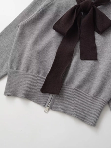 Detail of grey knitted cardigan featuring a large black bow and metallic silver zipper