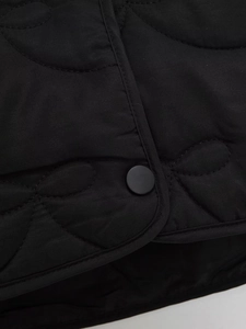 Detail of black quilted coat featuring floral pattern stitching and matte snap button
