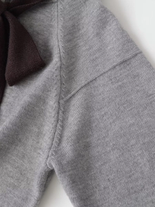 Close-up of grey knit cardigan fabric showing fine texture and delicate black bow detail