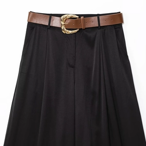 Détail du pantalon en satin noir avec ceinture marron et boucle dorée en spirale