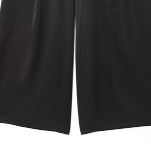 Détail du pantalon large en satin noir montrant la texture soyeuse et l'ourlet précis