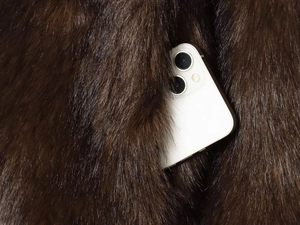 Detail of a deep brown faux fur jacket showing a functional side pocket with a phone