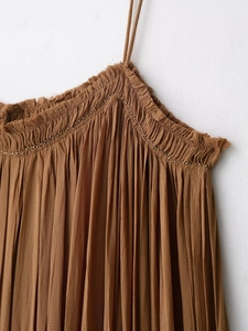 Detail of caramel pleated dress featuring ruffled neckline and delicate gold bead trim