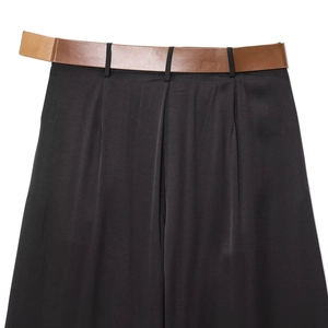 Détail d'un pantalon large en satin noir avec ceinture en cuir marron et taille plissée