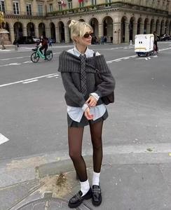 Outdoor street style view of a grey off-shoulder knit top paired with a pleated mini skirt