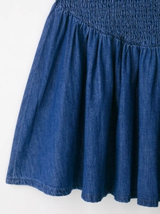 Dettaglio della vita elasticizzata a nido d'ape e dell'orlo pieghettato dell'abito in denim