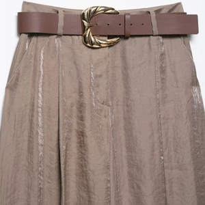 Gros plan d'un pantalon large en satin taupe avec ceinture en cuir et boucle dorée