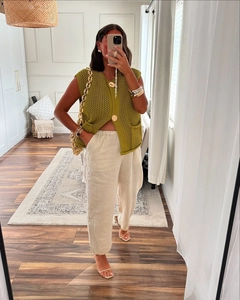 Detail of green chunky knit sleeveless top with large buttons and beige linen trousers