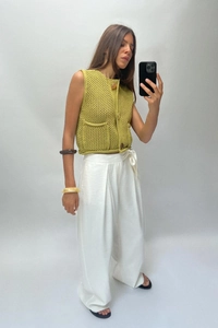 Macro detail of grass green knit vest with amber buttons and white wide-leg trousers