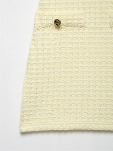 Nahaufnahme der hellgelben Waffelstrick-Textur und des goldenen Reliefknopfs am Kleid