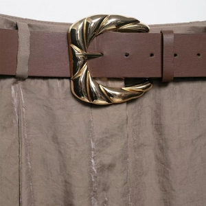 Détail d'une ceinture en cuir marron foncé avec boucle spirale dorée sur pantalon