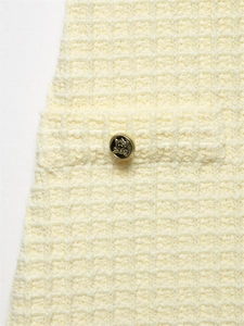 Makroaufnahme von cremefarbenem Tweed-Stoff mit Stricktextur und goldener Kronen-Knopf-Detail