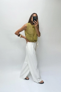 Detail view of olive green chunky knit sleeveless vest with buttons and white wide-leg trousers