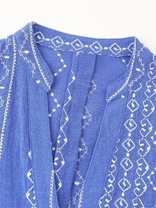 Détail de chemise bleue en coton et lin avec broderie bohème blanche sur col en V