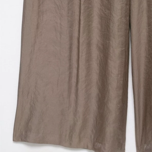 Détail montrant la texture satinée marron et le drapé fluide de ce pantalon large