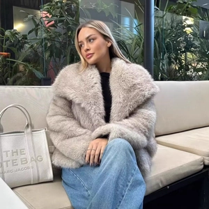 Elegante cappotto in ecopelliccia grigio chiaro con ampi baveri e jeans blu sul divano