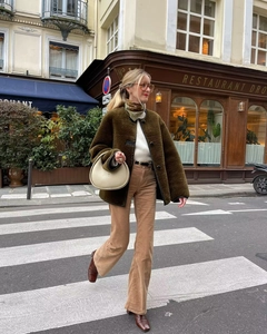Olive green faux fur jacket with black trim shown in a stylish street style setting