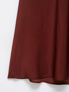 Détail macro de l'ourlet de robe midi bordeaux montrant le satin lisse et la couture