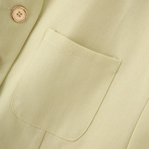 Macro detail of linen vest featuring a patch pocket and a gold-rimmed decorative button