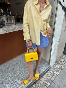 Outfit estivo chic con camicia a righe gialle, pantaloncini blu e borsa in pelle coordinata