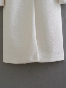 Detailed macro view of soft white wool blend fabric and hem stitching on long coat
