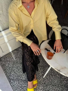Dettaglio camicia a righe gialle con gonna in pizzo nero e collana con croce d'argento