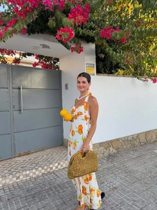 Halter neck backless maxi dress with orange fruit print shown in a vacation street setting