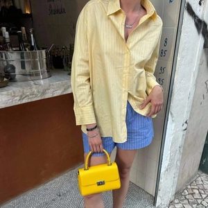 Camicia a righe gialle da donna con pantaloncini blu e borsa a mano in pelle gialla