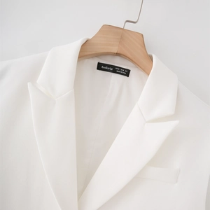 Dettaglio del colletto del blazer bianco e dell'etichetta Aveloria su una gruccia