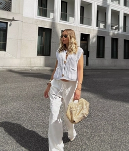 Detailed view of white chunky knit vest with large gold buttons and woven texture