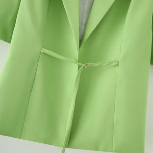 Detail of grass green blazer featuring a waist belt with golden metal ring closure