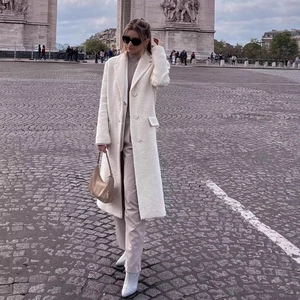 Long cream-colored wool coat with classic lapels and pockets in front of the Arc de Triomphe