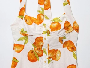 Detail of linen summer dress featuring orange citrus print with heart-shaped neckline and buttons
