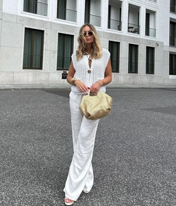 Detail of white crochet knit vest with V-neck and button on a model's summer outfit