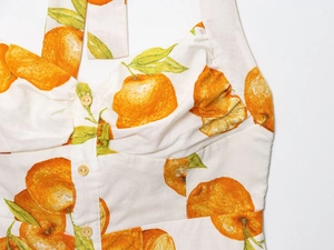 Detailed close-up of orange fruit print and button details on linen summer dress