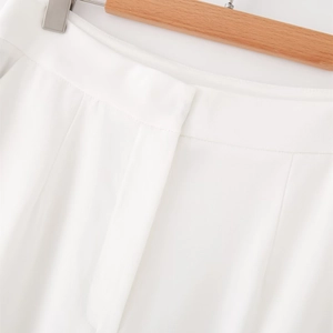 Dettaglio dei pantaloni bianchi con texture in saia e sartoria pulita in vita