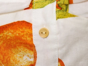 Detail shot of linen dress fabric featuring orange prints and natural wooden button
